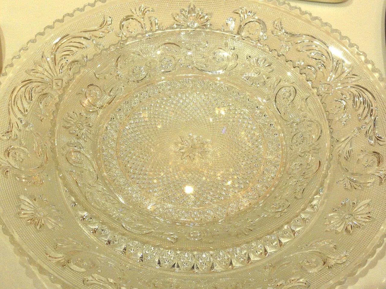 Plat rond en cristal incolore, décoré en relief de rinceaux, de fleurs et d’un fond pointillé, avec une étoile au centre