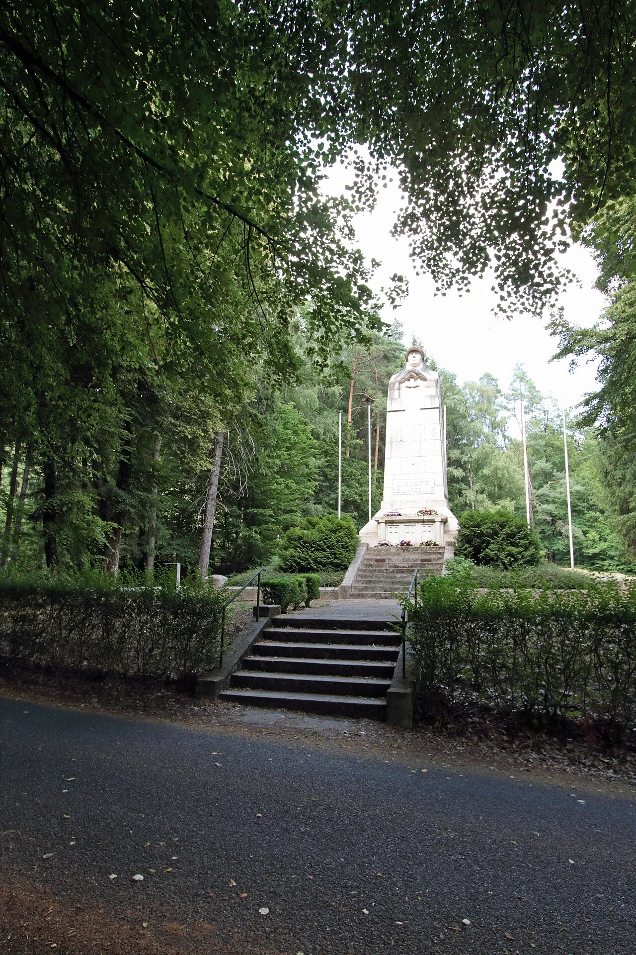 Le monument-ossuaire de la Haute-Chevauchée en haut d’un escalier, sous les arbres : un obélisque blanc surmonté d’un soldat casqué, mains posées sur une épée