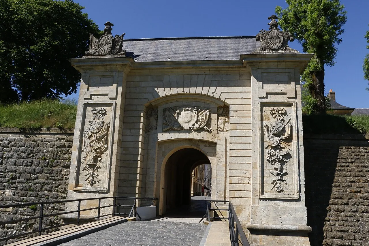 La porte de France de Longwy : portail de pierre à arcade orné de trophées sculptés, précédé d’un pont qui franchit le fossé