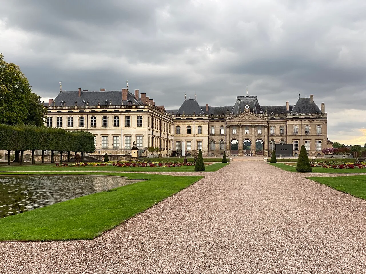 Le château de Lunéville vu depuis les jardins des Bosquets : allée de gravier, bassin, pelouses et façades sous un ciel gris