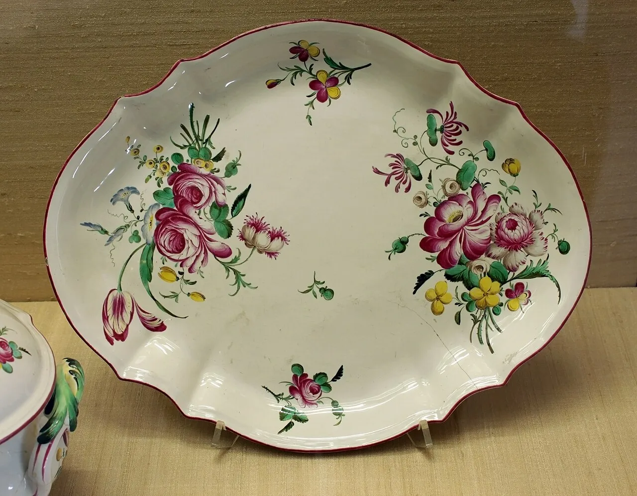 Plat ovale chantourné en faïence blanche, bordé de rouge, peint de bouquets de roses, de tulipes et de fleurs des champs