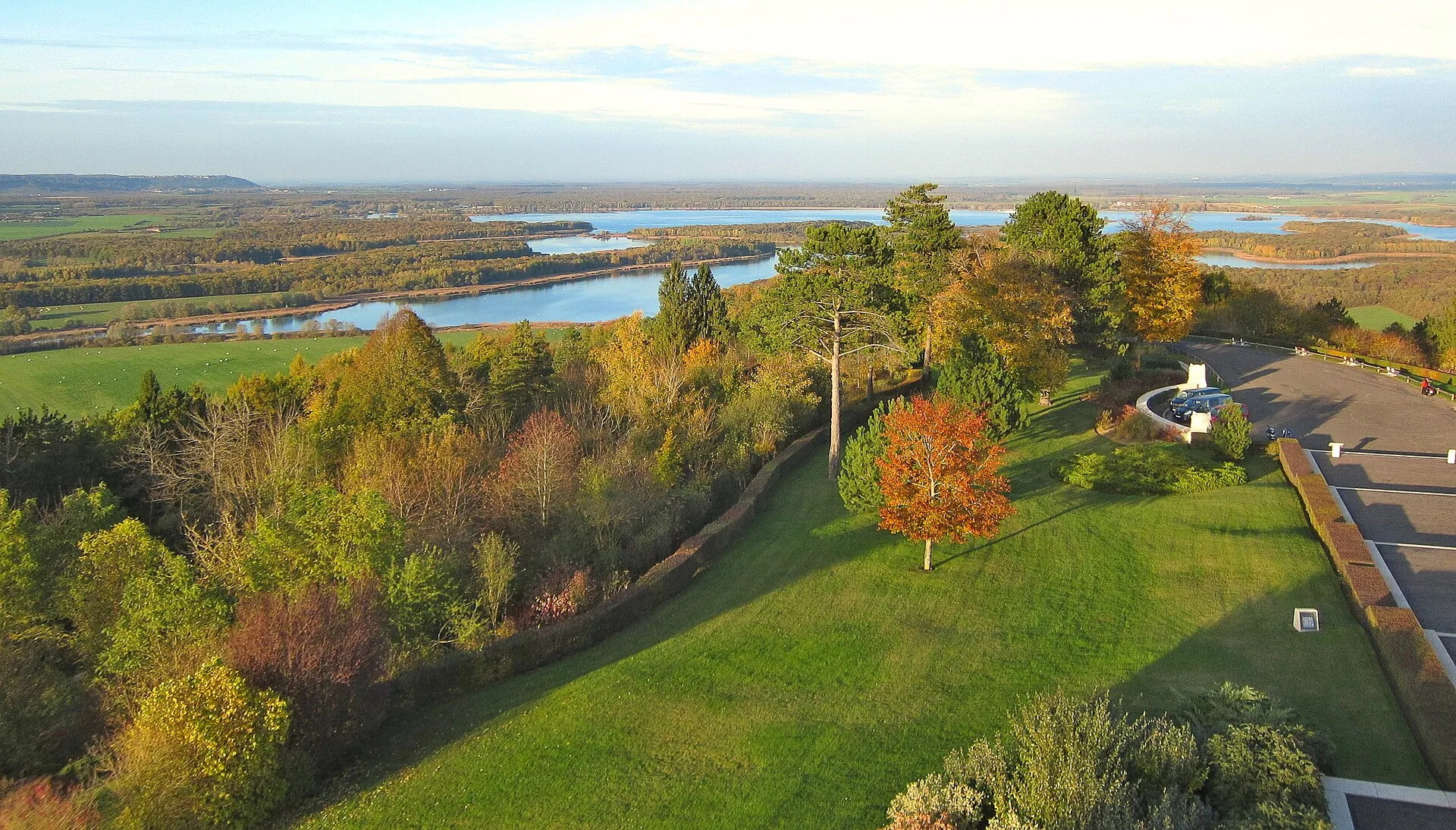 Vue aérienne d’automne depuis la butte de Montsec : arbres roux au premier plan, le lac de Madine qui s’étire dans la plaine