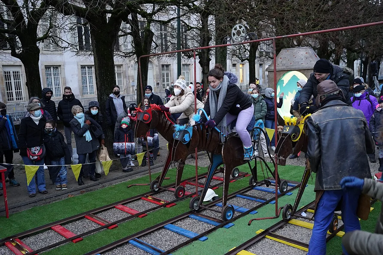 Une course de chevaux de bois montés sur rails, avec des participants emmitouflés, devant un public en manteaux d’hiver