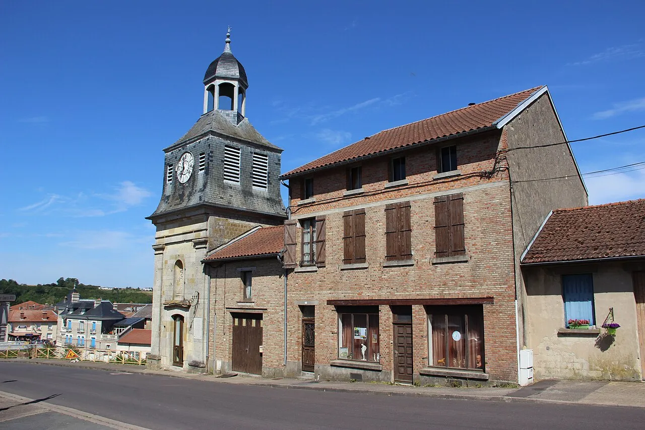 La tour de l’Horloge de Varennes, coiffée d’ardoise et d’un lanternon, à côté d’une maison de briques aux volets bruns, sous un ciel bleu